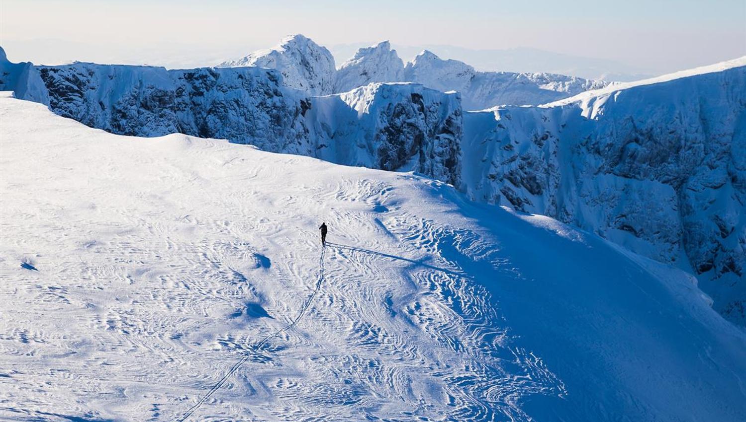 Bergskiläufer auf einem Plateau mit Abgründen und spitzen Gipfeln im Hintergrund