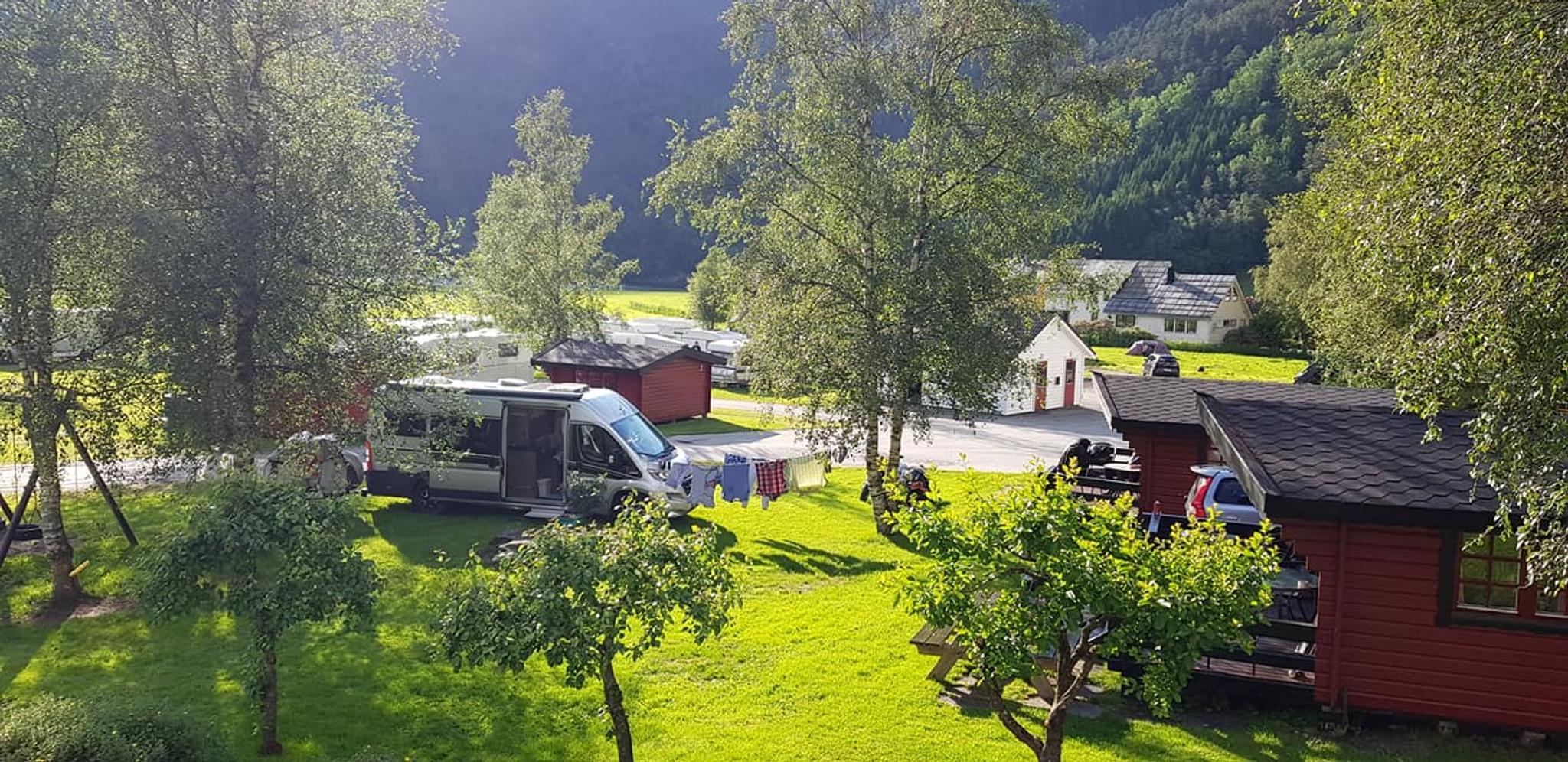 Sunny day at Folgefonn Cabins and Farm Camping in Hardanger, with red cabins, campervans, and lush green surroundings.