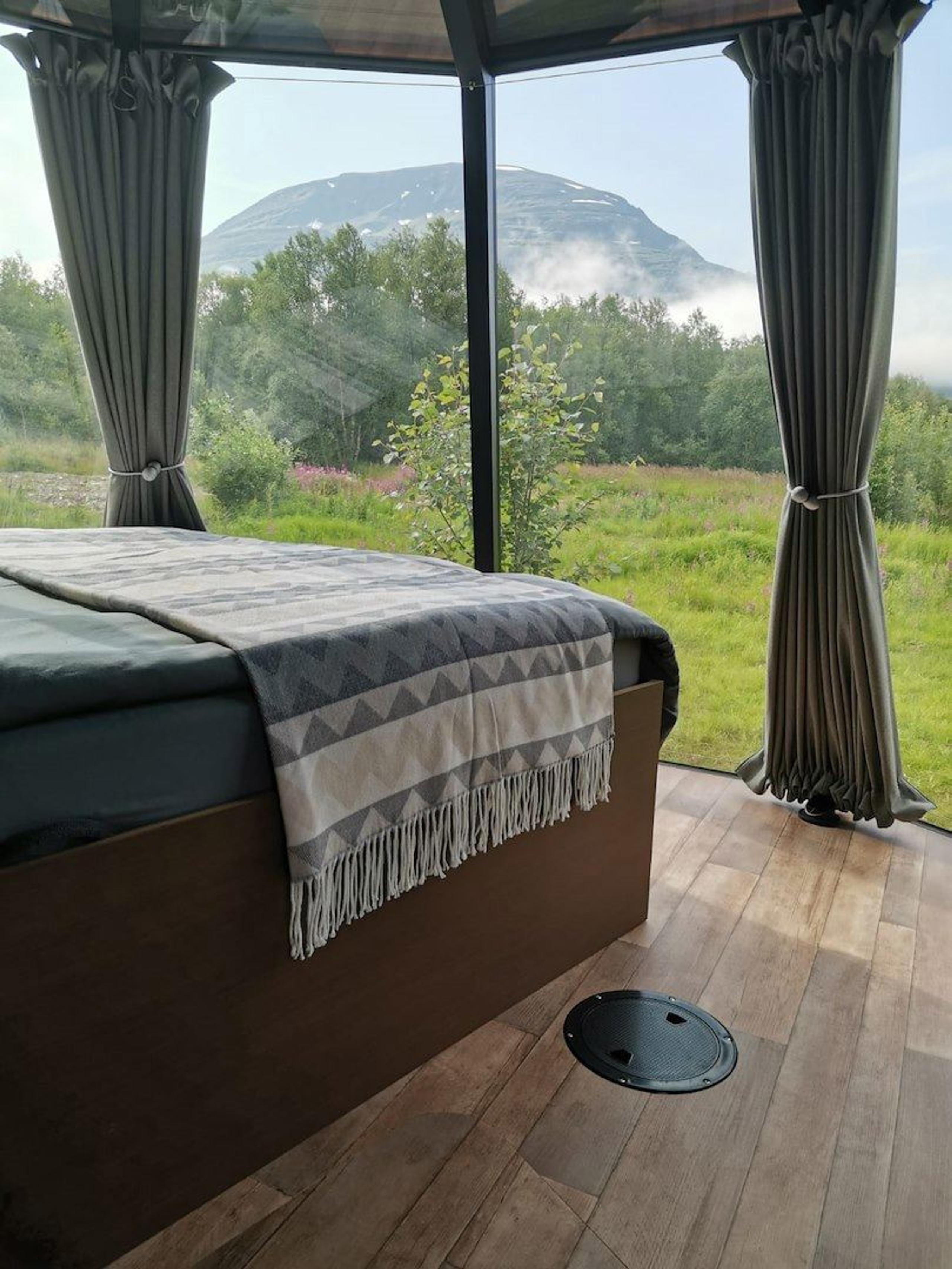 A bed and panoramic windows inside a glass igloo overlooking the surrounding nature at North Experience.