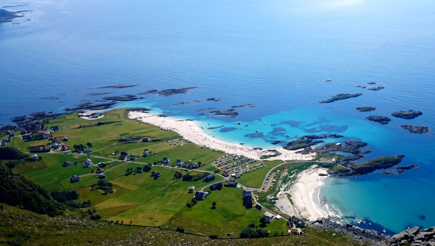 Grotlesanden. Aerial view of a green coastal village with roads and houses beside white-sand beaches and turquoise water with rocky islets..