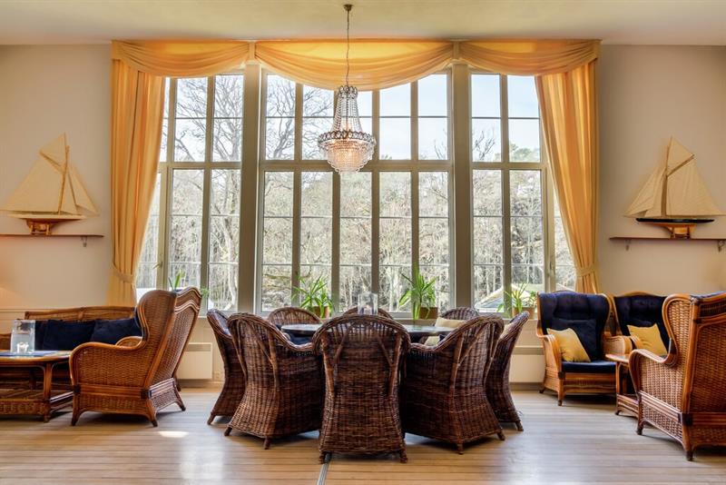 Lys og innbydende salong på Hankø Hotell & Spa, med store vinduer, kurvstoler, sofa og maritime detaljer.
