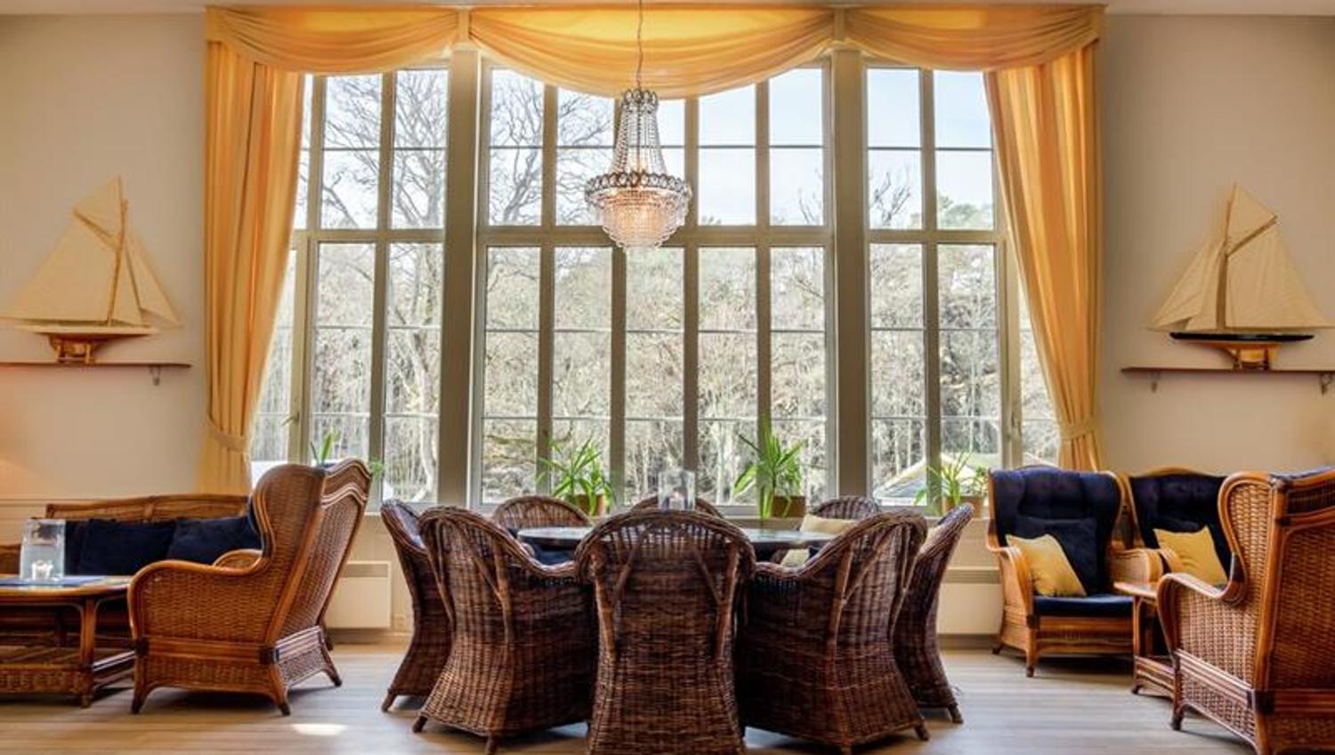Lys og innbydende salong på Hankø Hotell & Spa, med store vinduer, kurvstoler, sofa og maritime detaljer.