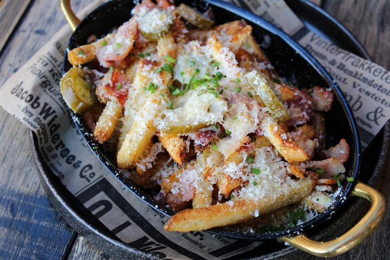 Fries served with cheese, bacon and garnish in a pan. The dish is offered as a sharing plate or bar food.