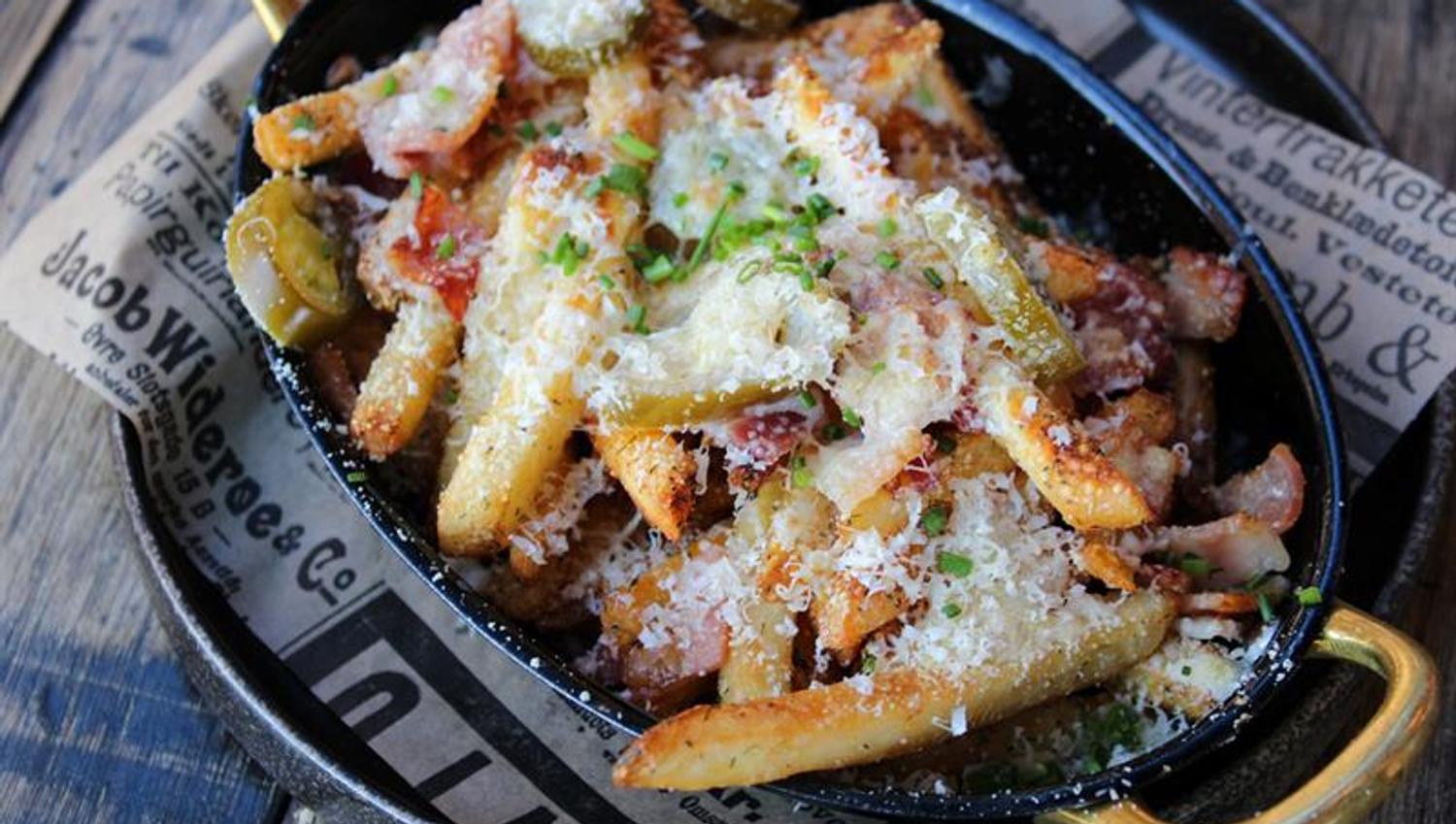 Fries served with cheese, bacon and garnish in a pan. The dish is offered as a sharing plate or bar food.