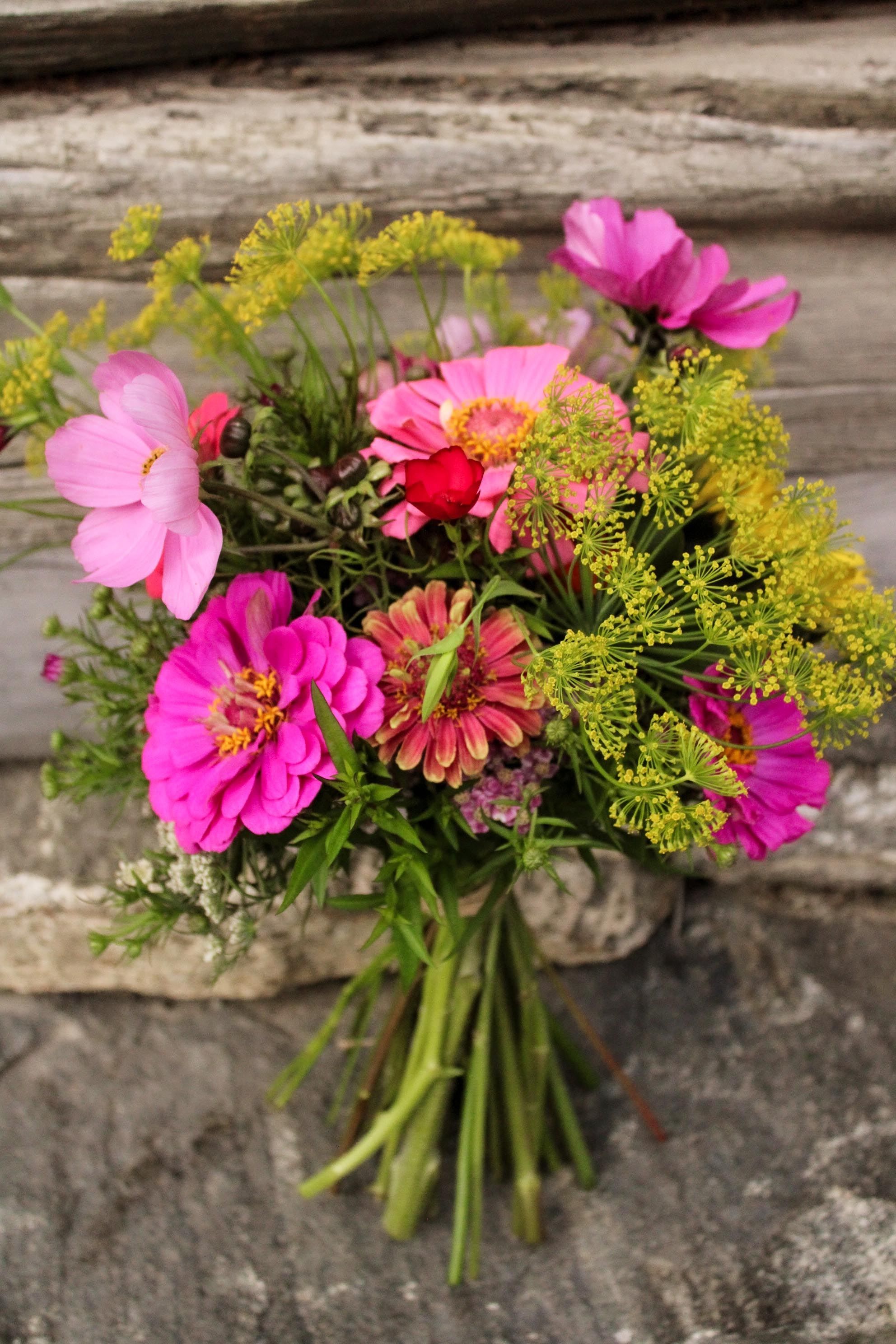 Colorful bouquet of pink and magenta flowers with green stems resting on weathered wooden boards and stone..