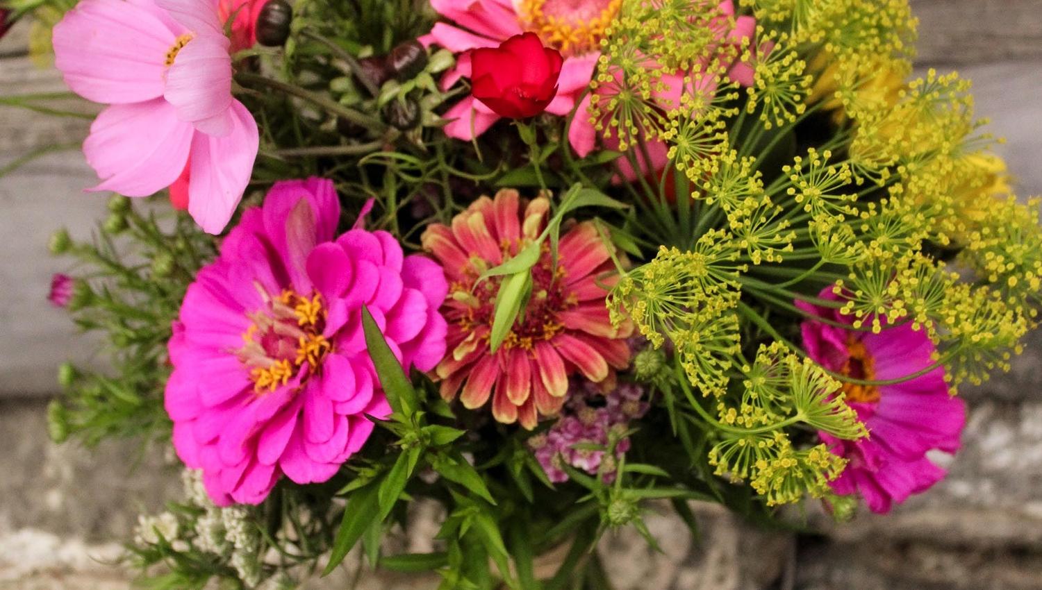 Colorful bouquet of pink and magenta flowers with green stems resting on weathered wooden boards and stone..