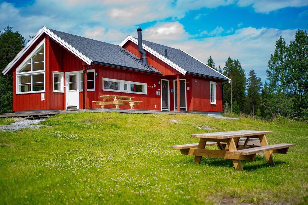 The red Østtorphytta. In the foreground – green grass and a picnic table. Photo.