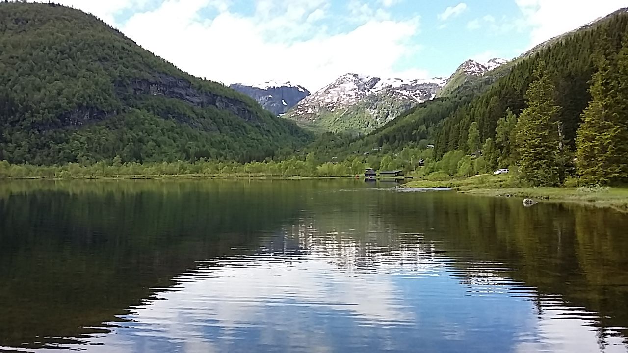 Beautiful view of Lake Fitjadalsvatnet in Hardanger, with green hills and snow-capped peaks reflecting in the water.