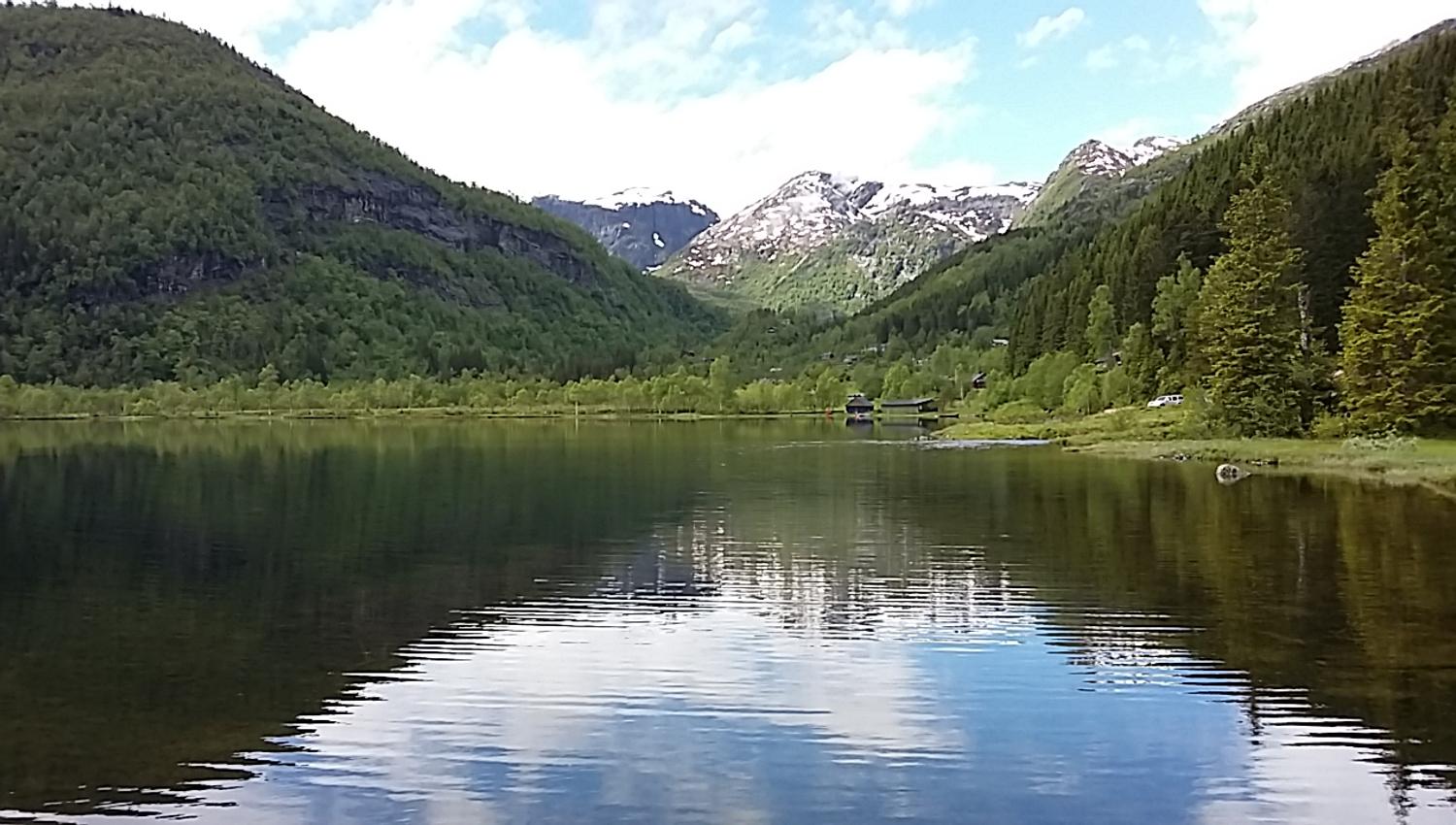Beautiful view of Lake Fitjadalsvatnet in Hardanger, with green hills and snow-capped peaks reflecting in the water.