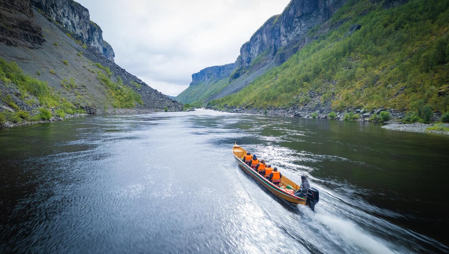 Un bateau navigue sur une rivière entourée de falaises verdoyantes.