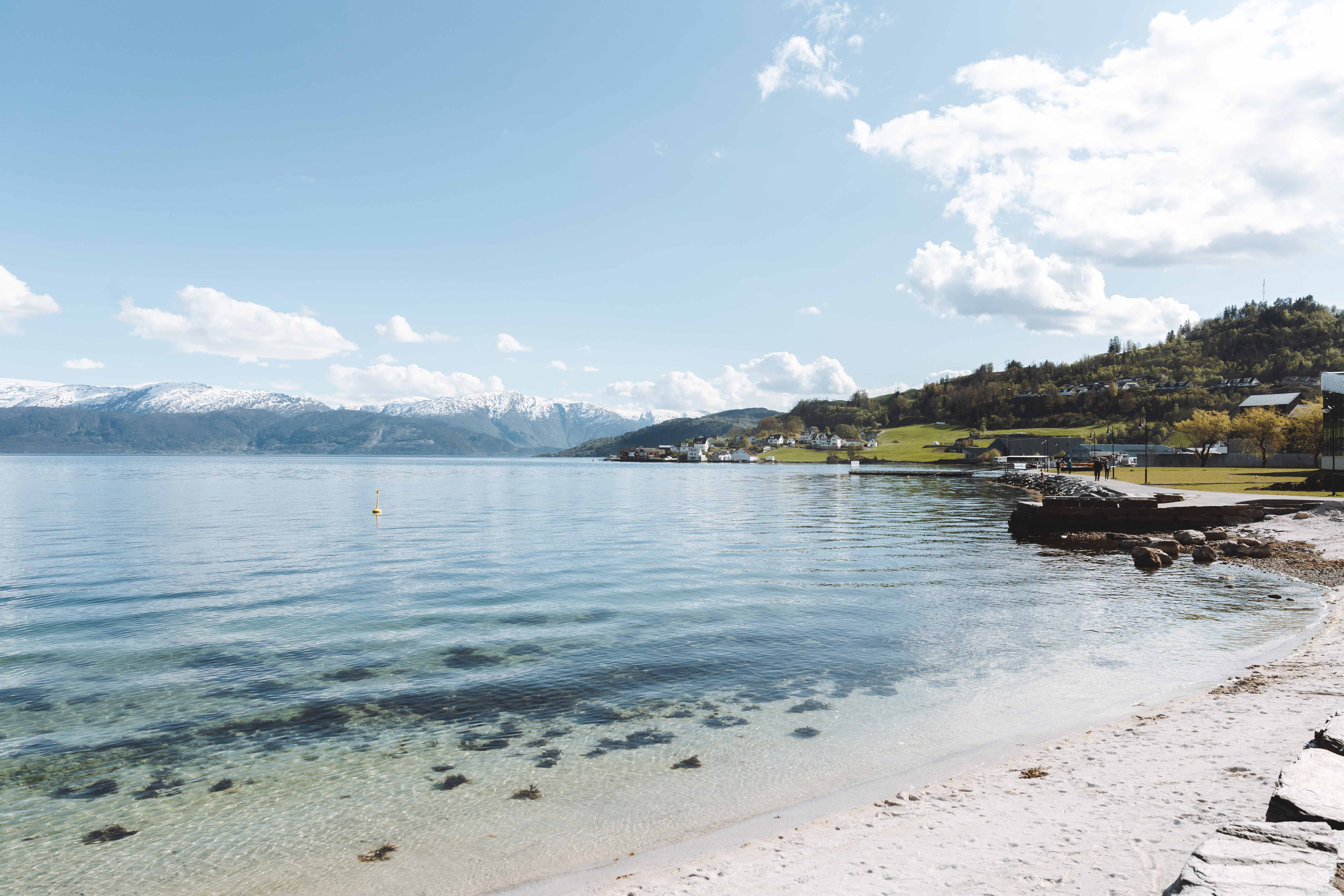 Tranquil shoreline with clear waters and snow-capped mountains in the distance.