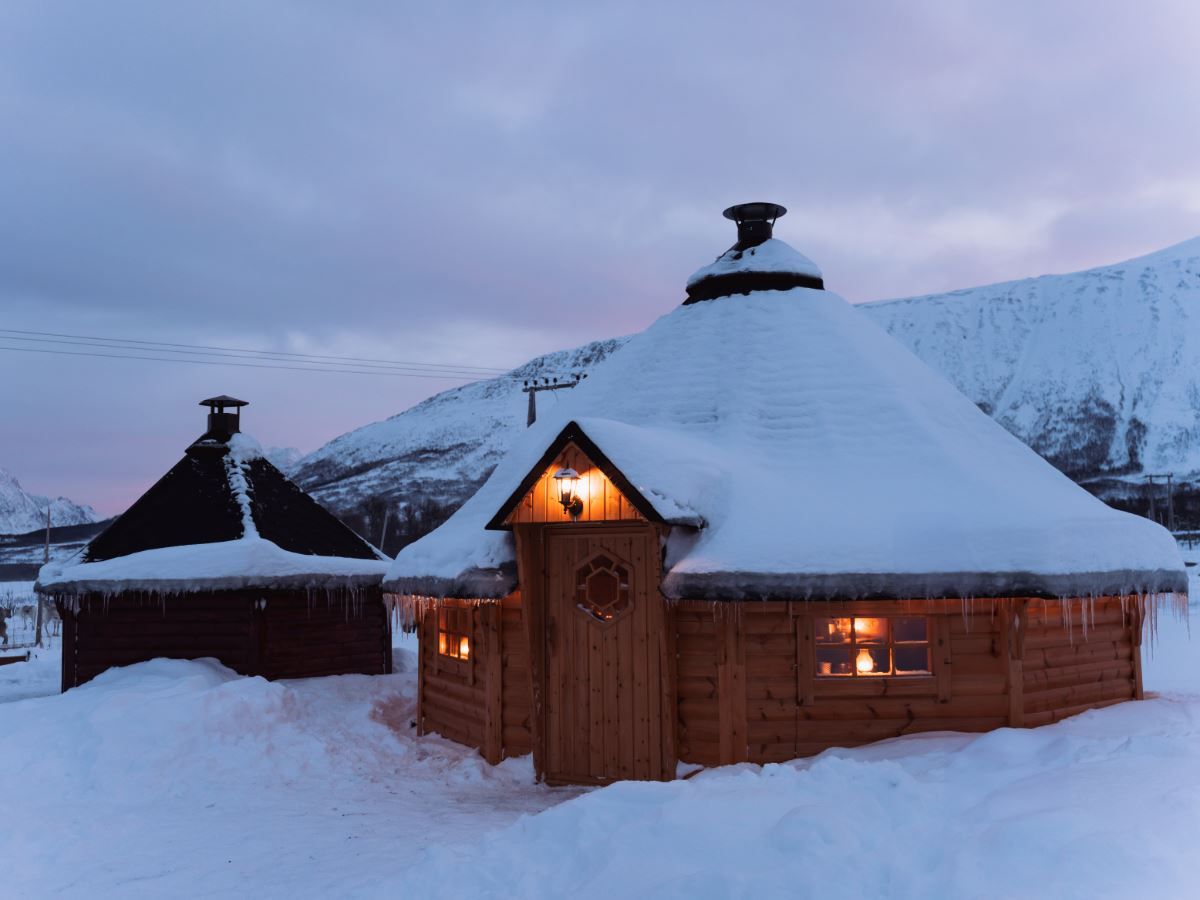 Snow-covered lavvus at Tromsø Lapland’s Sámi camp, surrounded by mountains and winter scenery.