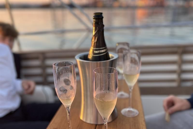A glass of sparkling wine is served on deck with a view of the harbour at sunset.