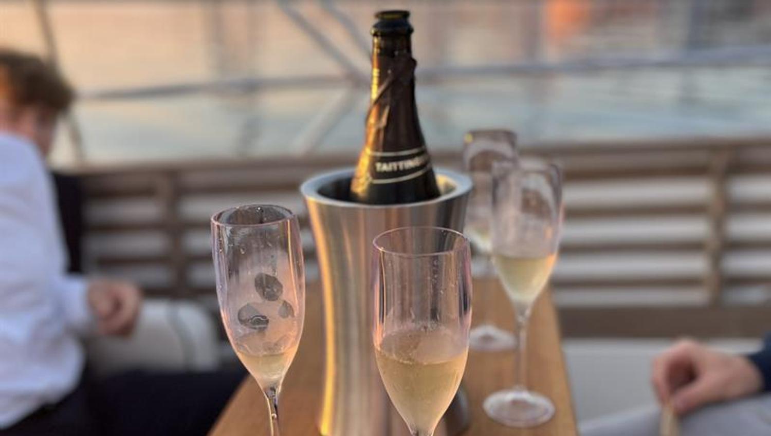 A glass of sparkling wine is served on deck with a view of the harbour at sunset.