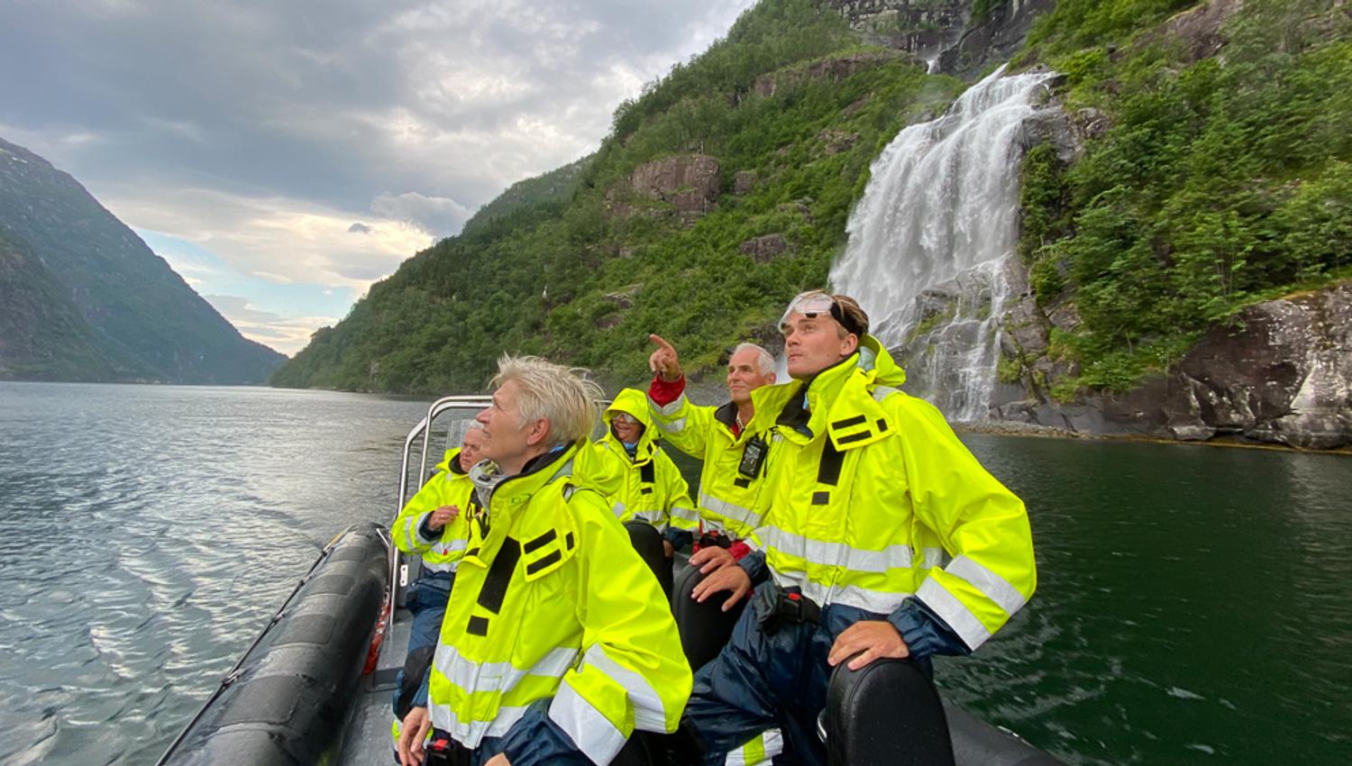 Tourists in yellow suits gaze in awe at an impressive waterfall from the RIB boat in the Hardangerfjord.