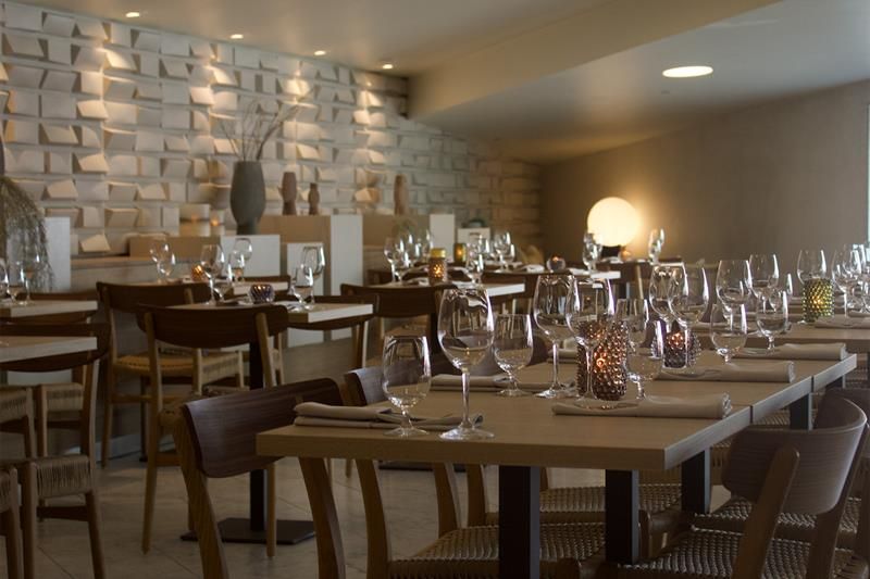 Interior with tables set for dining and chairs, light beige floor and a wall made out of stone.