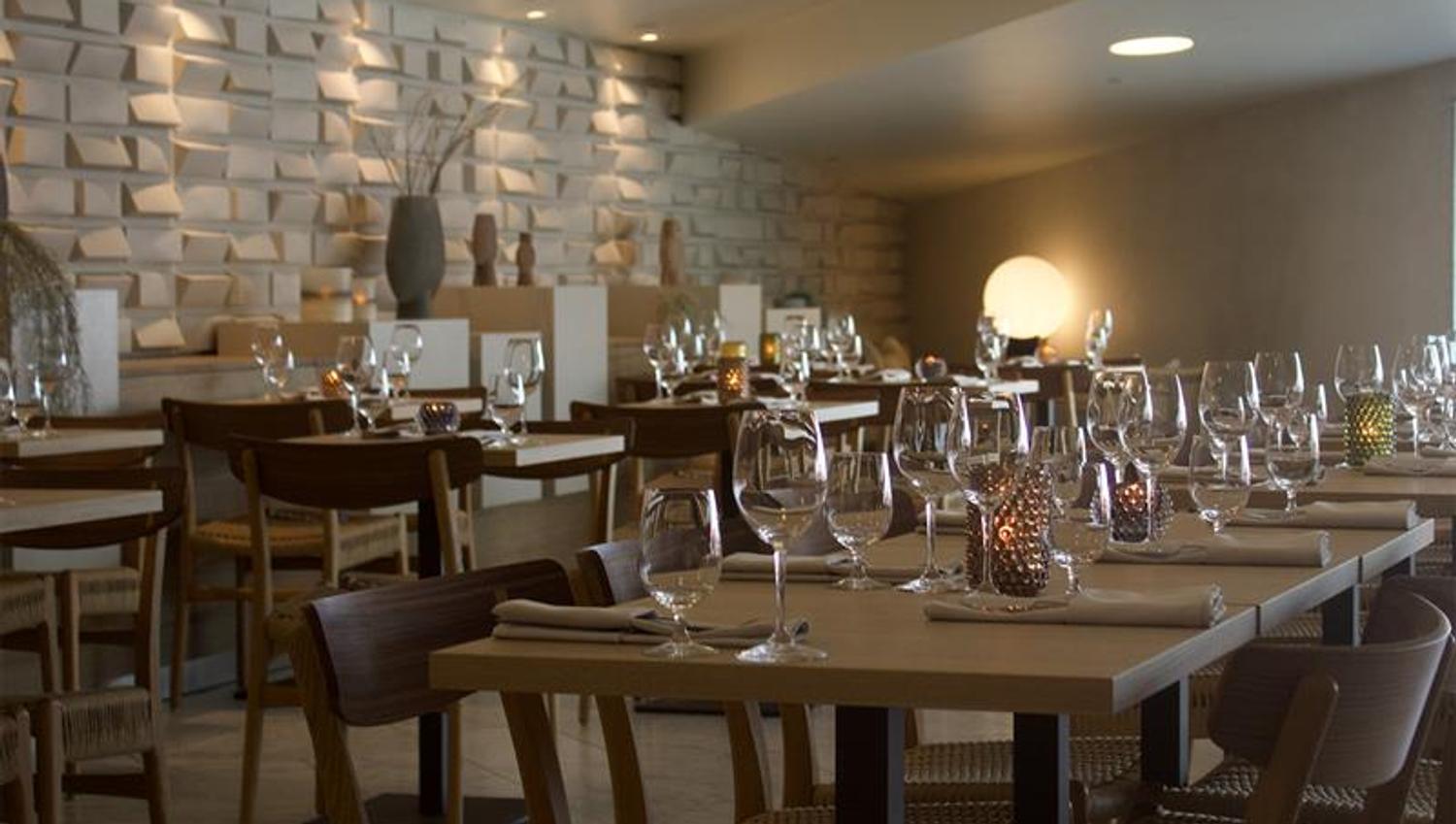 Interior with tables set for dining and chairs, light beige floor and a wall made out of stone.