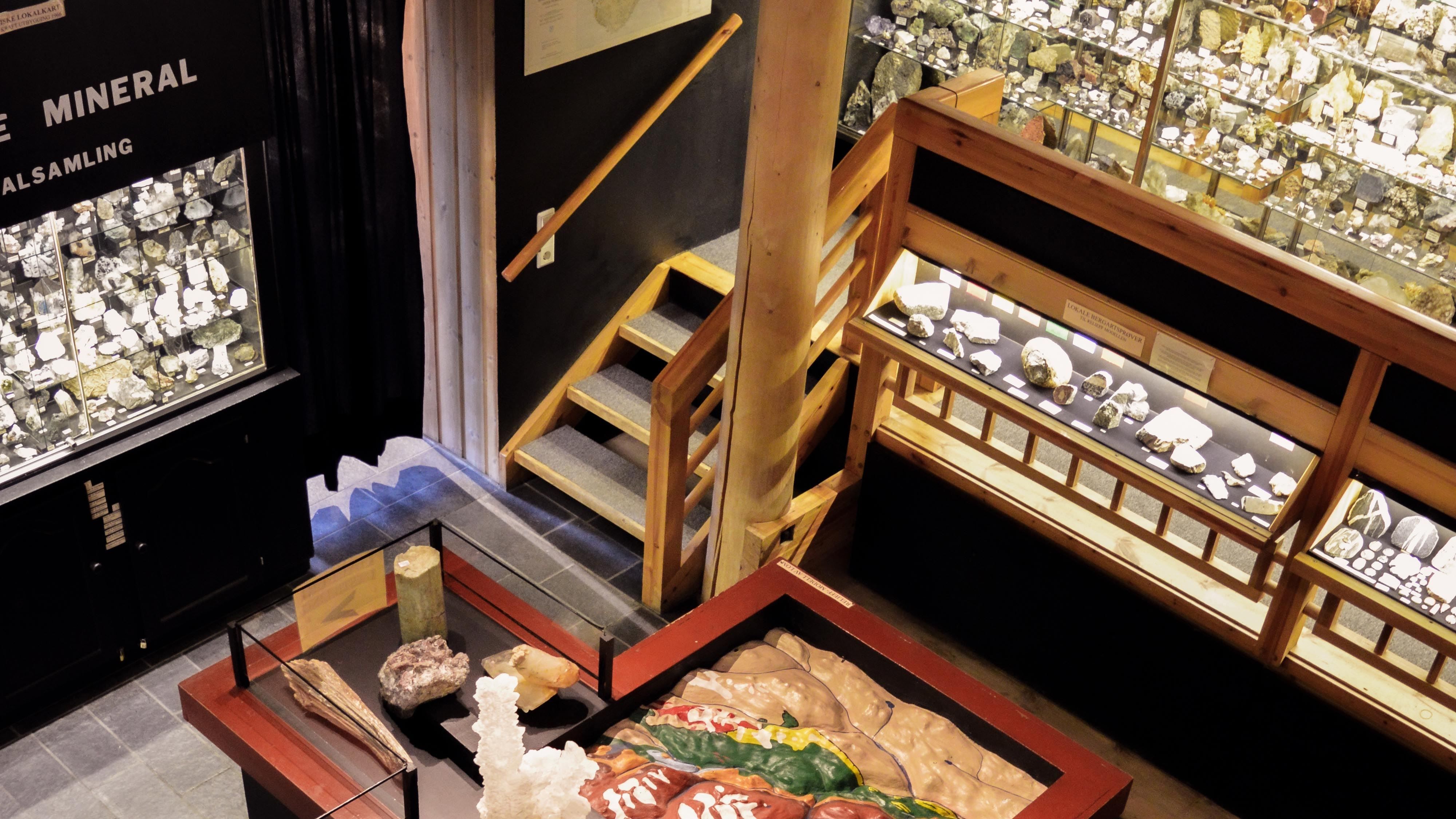 Overhead view of a museum mineral gallery with wooden stairs, glass display cases, and rock specimens on tables..
