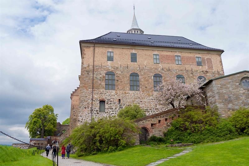 Akershus Castle seen from a worm's-eye view, with people walking alongside it one left hand side.