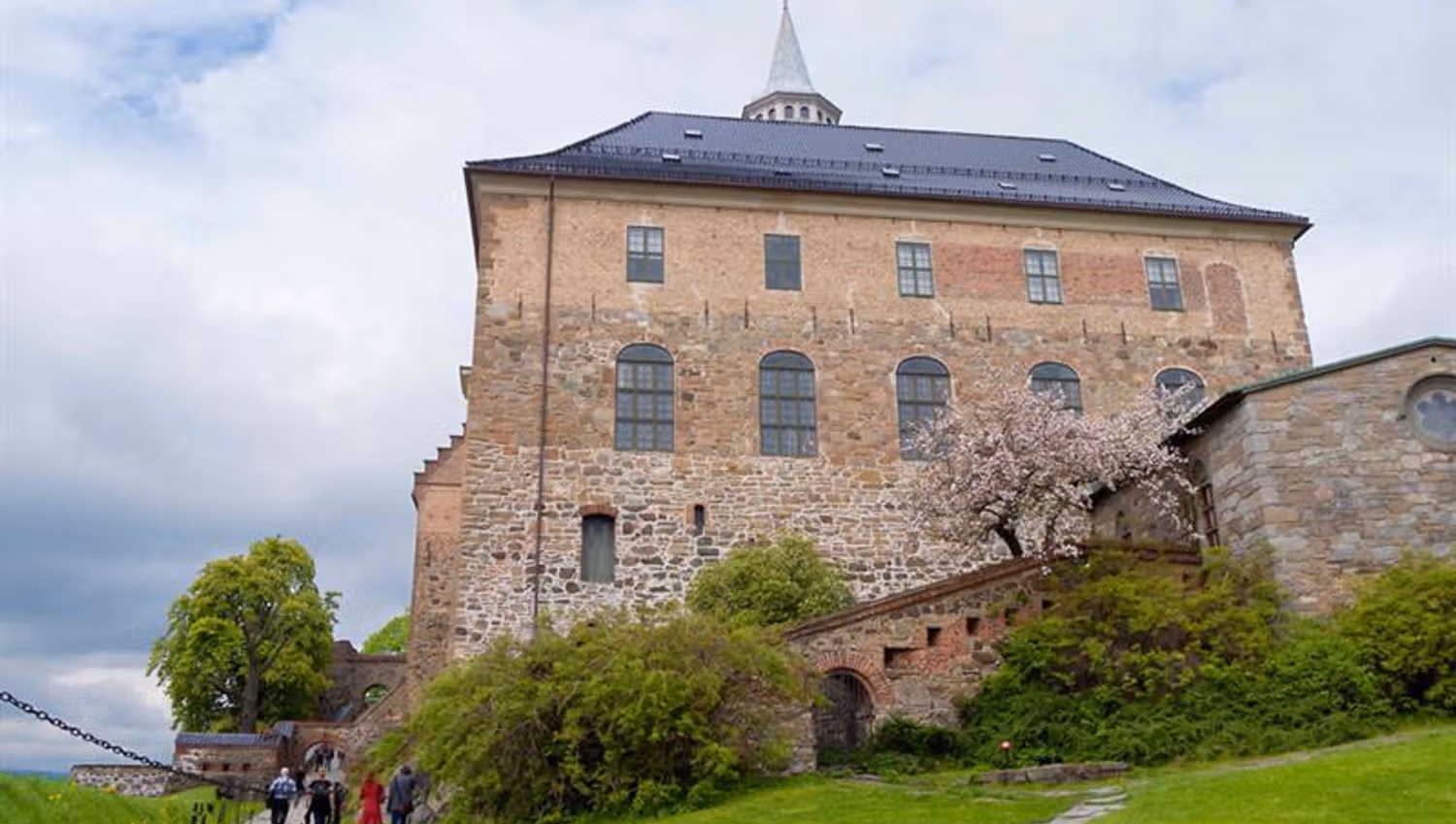 Akershus Castle seen from a worm's-eye view, with people walking alongside it one left hand side.