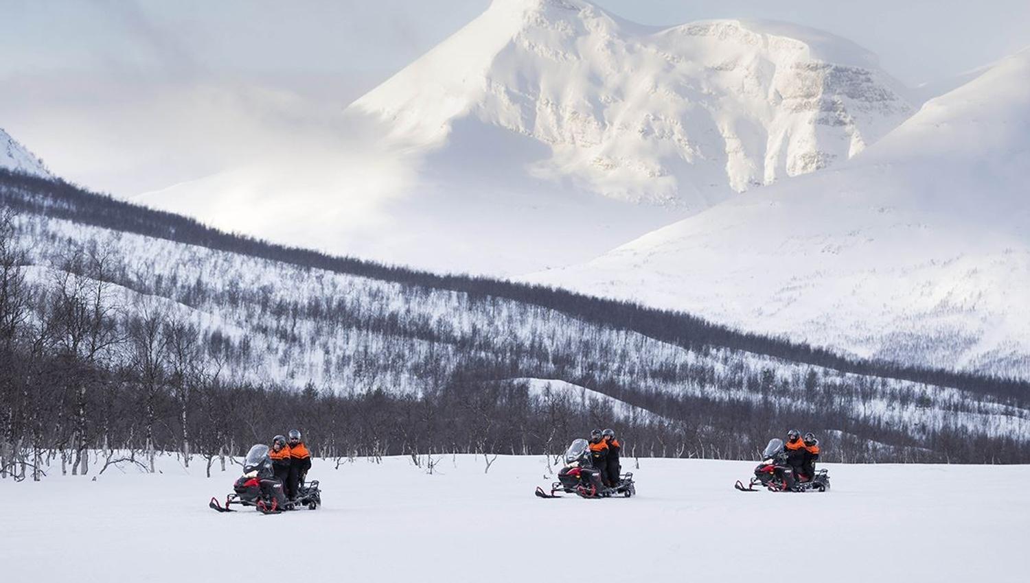 Three snow scooters drive past massive mountains