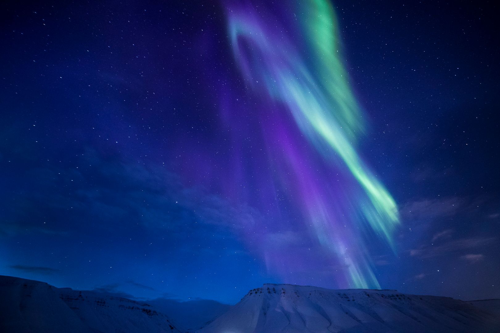 Purple and green northern lights above the mountains