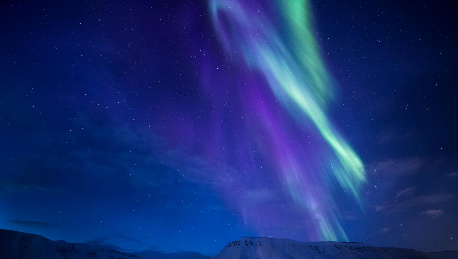 Purple and green northern lights above the mountains