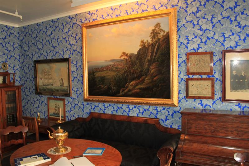 Picture inside from one of the living rooms. An old rococo sofa in black velvet under a large nature painting on a wall wallpapered with blue and gray