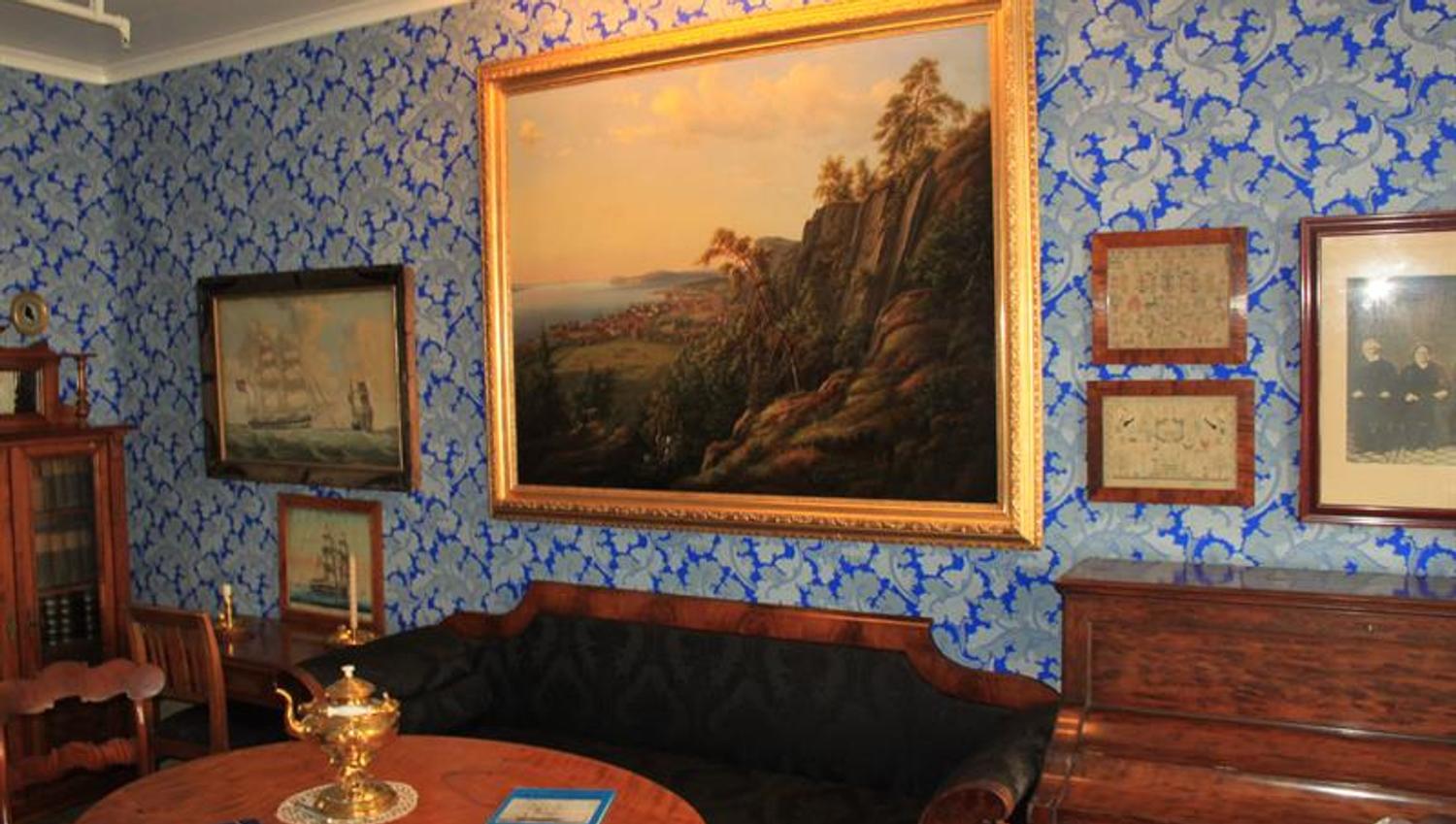Picture inside from one of the living rooms. An old rococo sofa in black velvet under a large nature painting on a wall wallpapered with blue and gray