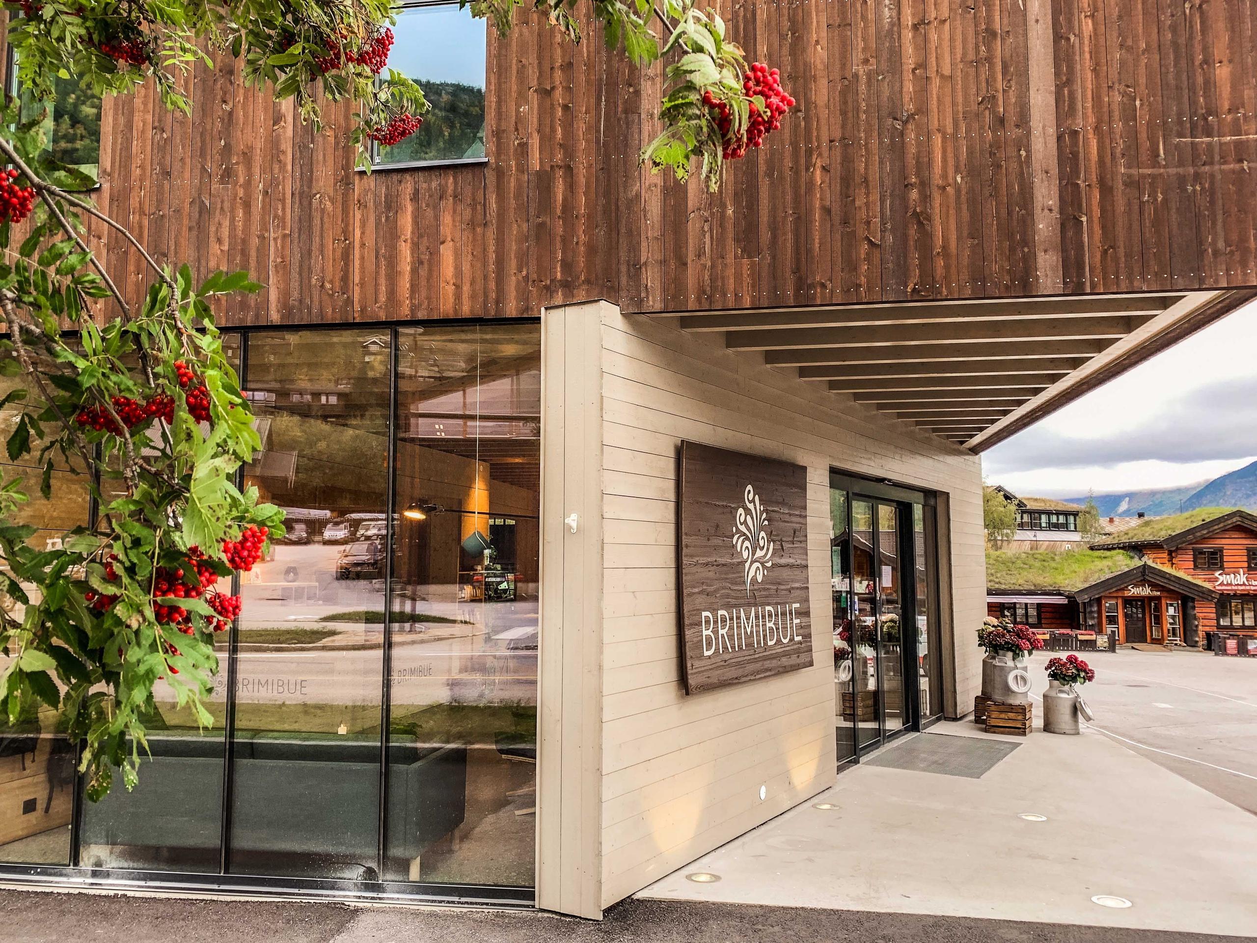 Wood-clad building entrance with large glass windows, a sign on the wall, and red berries hanging in foreground..
