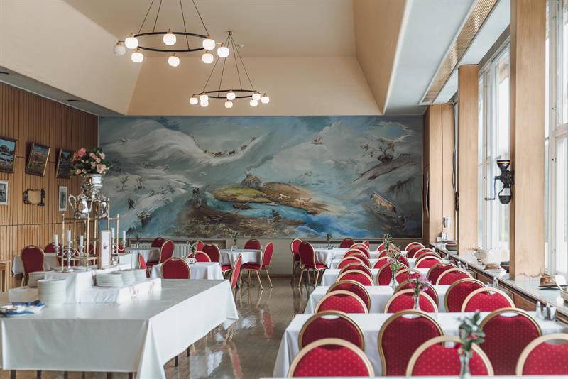 The dining room with red chairs and a large wall painting in the background.