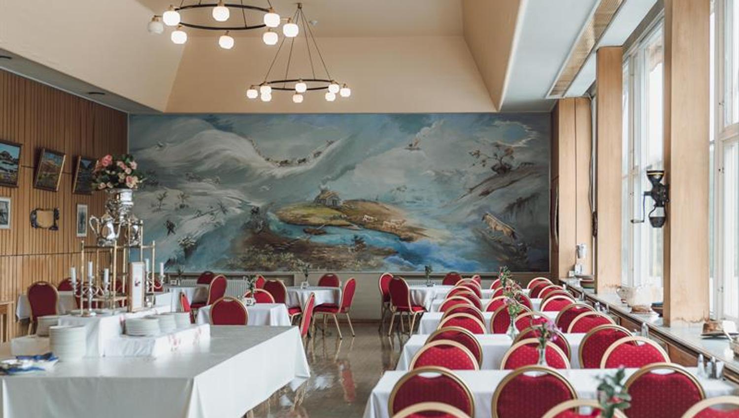 The dining room with red chairs and a large wall painting in the background.