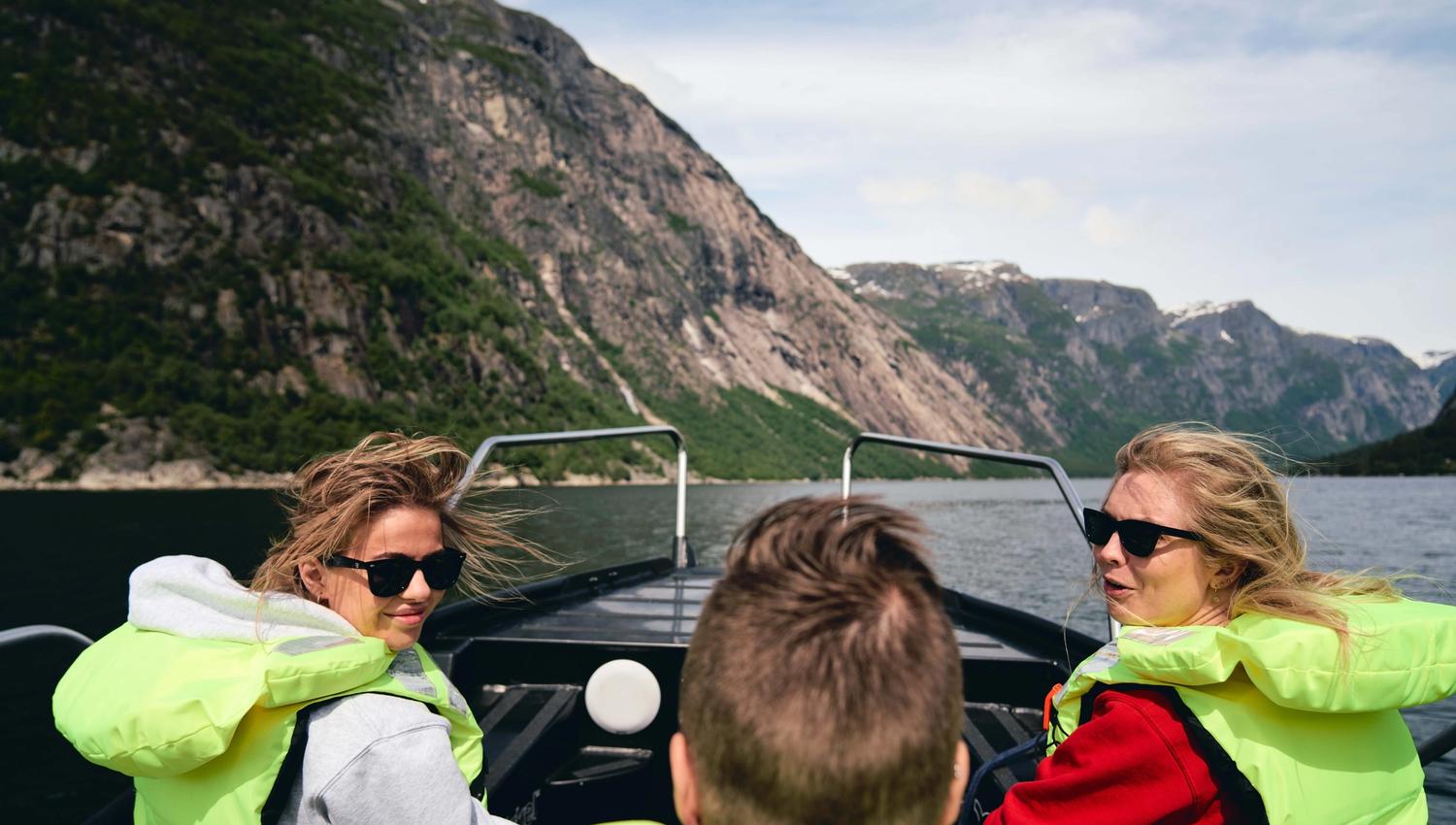 Three passengers with wind in their hair laughing onboard the boat.