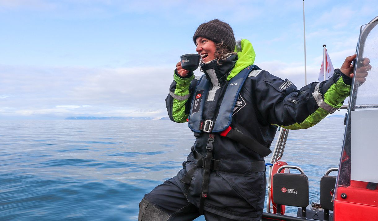 A smiling guide on board a RIB boat on a fjord having a cup of something hot to drink