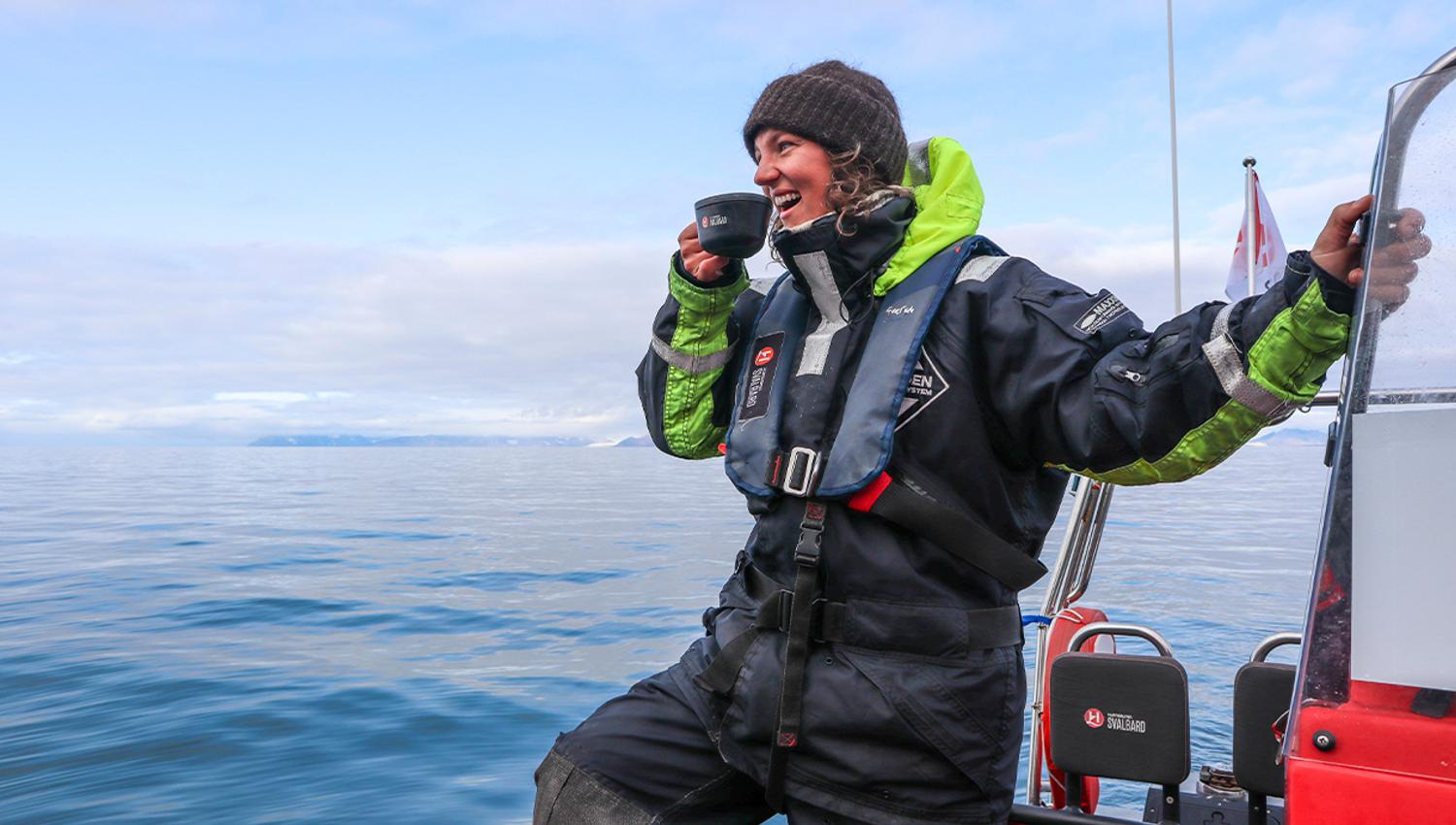A smiling guide on board a RIB boat on a fjord having a cup of something hot to drink