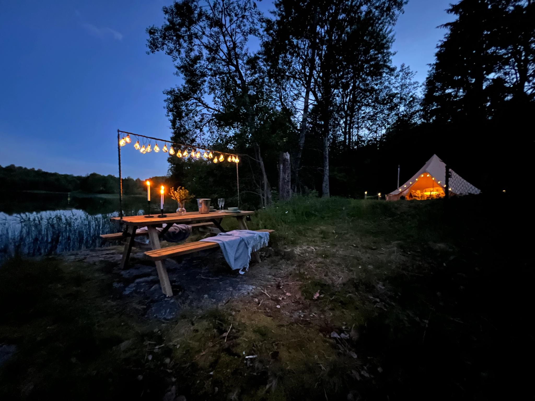Mood picture outside the glamping tent, with a covered picnic table and a view out towards the lake.