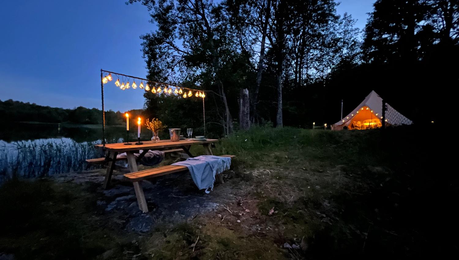 Mood picture outside the glamping tent, with a covered picnic table and a view out towards the lake.
