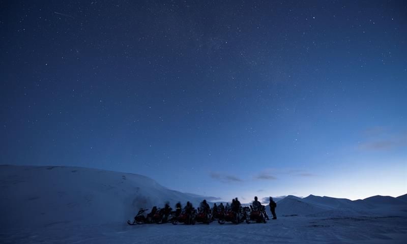 Mørkeblå nattehimmel med en gruppe mennesker og snøscootere