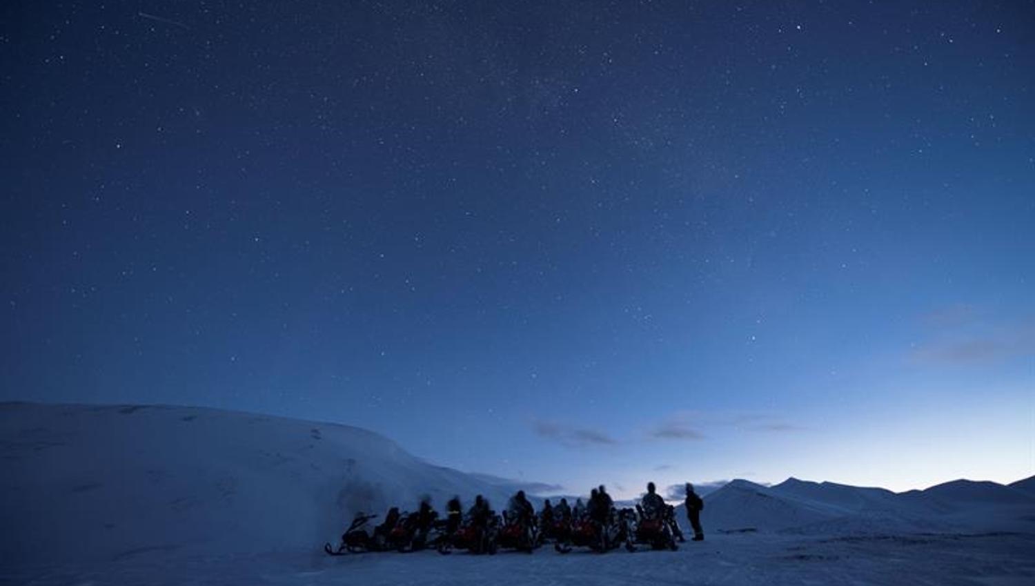 Mørkeblå nattehimmel med en gruppe mennesker og snøscootere