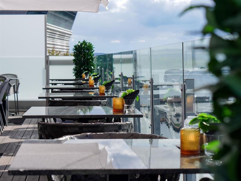Stylish rooftop terrace with tables, glass railings and views towards the fjord.