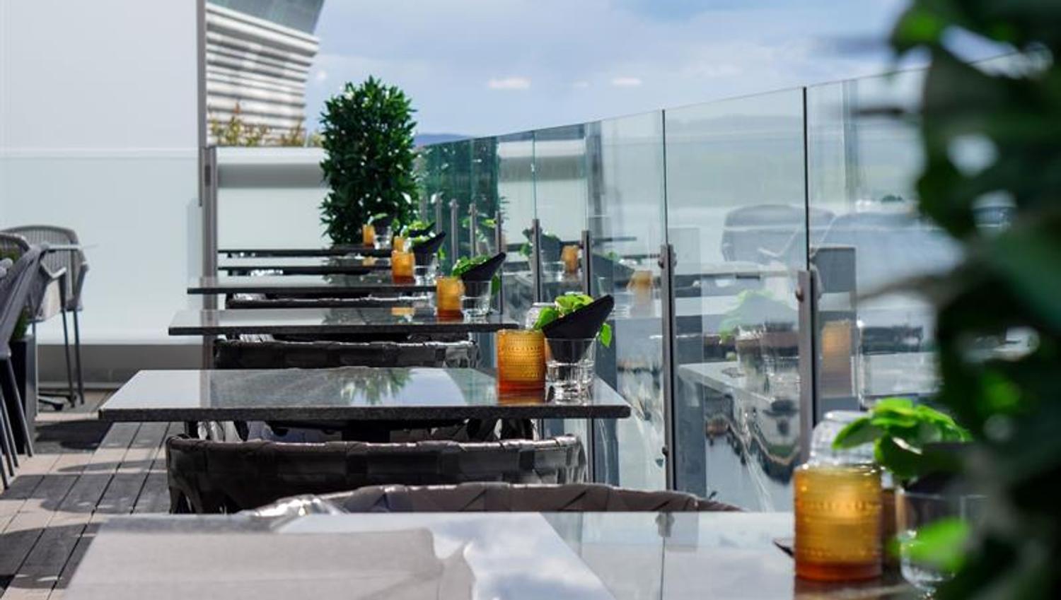 Stylish rooftop terrace with tables, glass railings and views towards the fjord.
