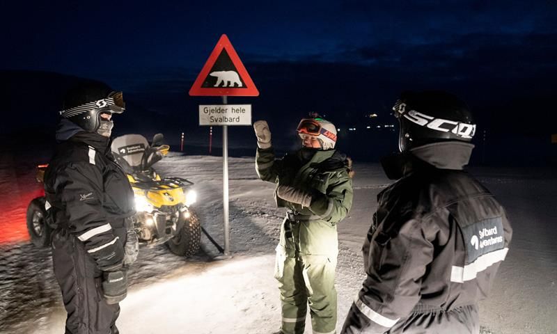 tre mennesker står ved isbjørnskiltet med ATV ved siden av
