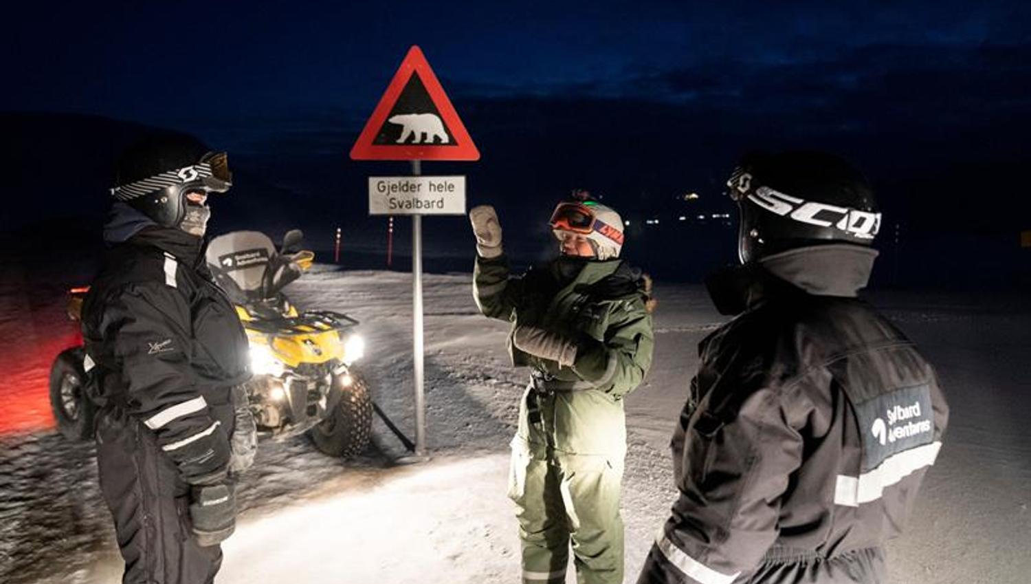 tre mennesker står ved isbjørnskiltet med ATV ved siden av