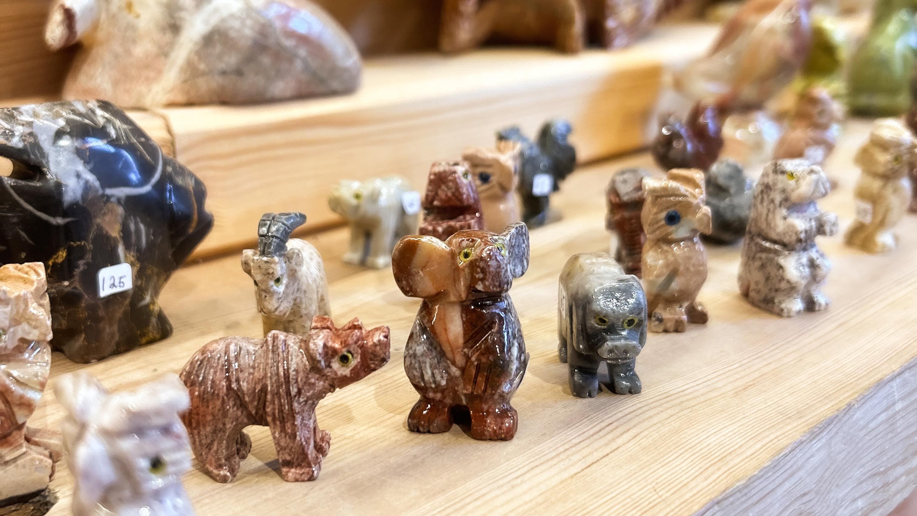 Assorted small carved stone animal figurines arranged on a wooden shelf, with several bears in the foreground..