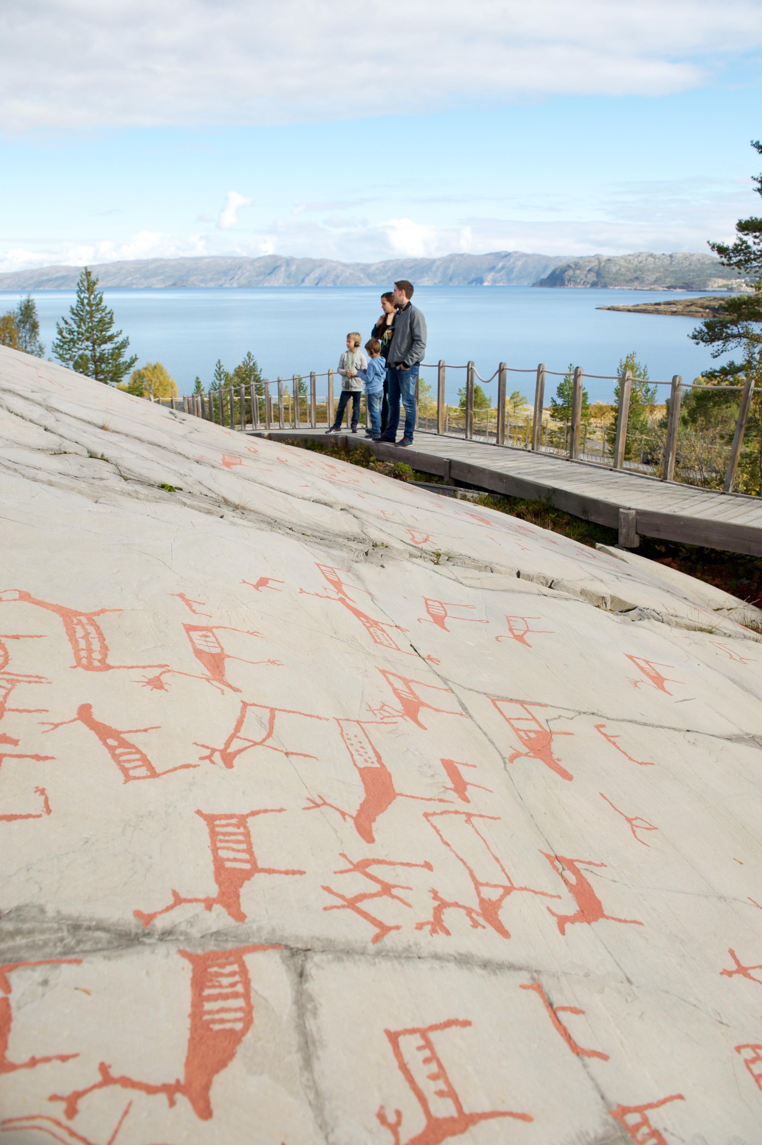 Pétroglyphes rouges sur une roche, avec des visiteurs admirant le paysage en arrière-plan.