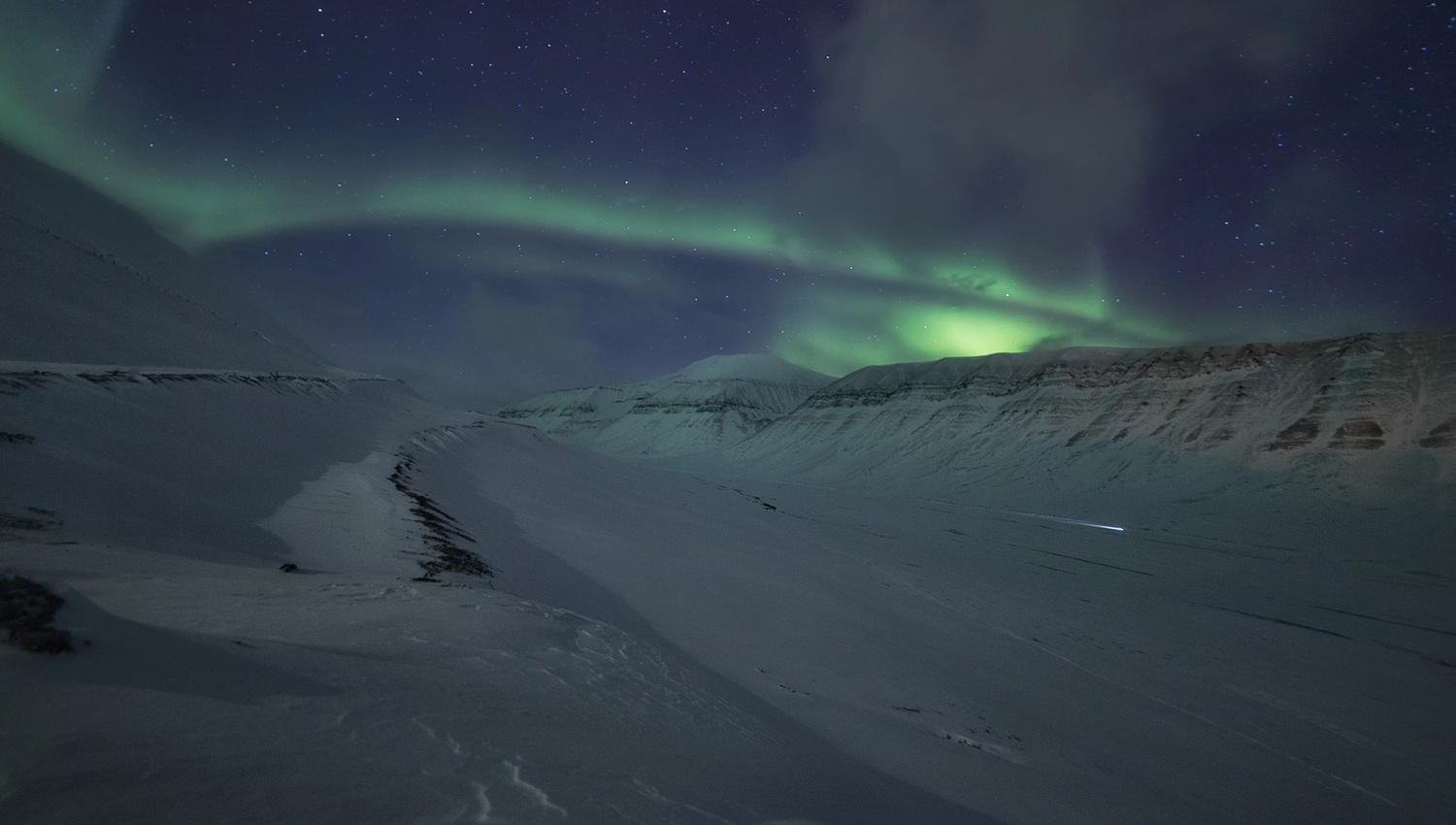 Snødekte fjell og dal, med nordlys himmelen over.
