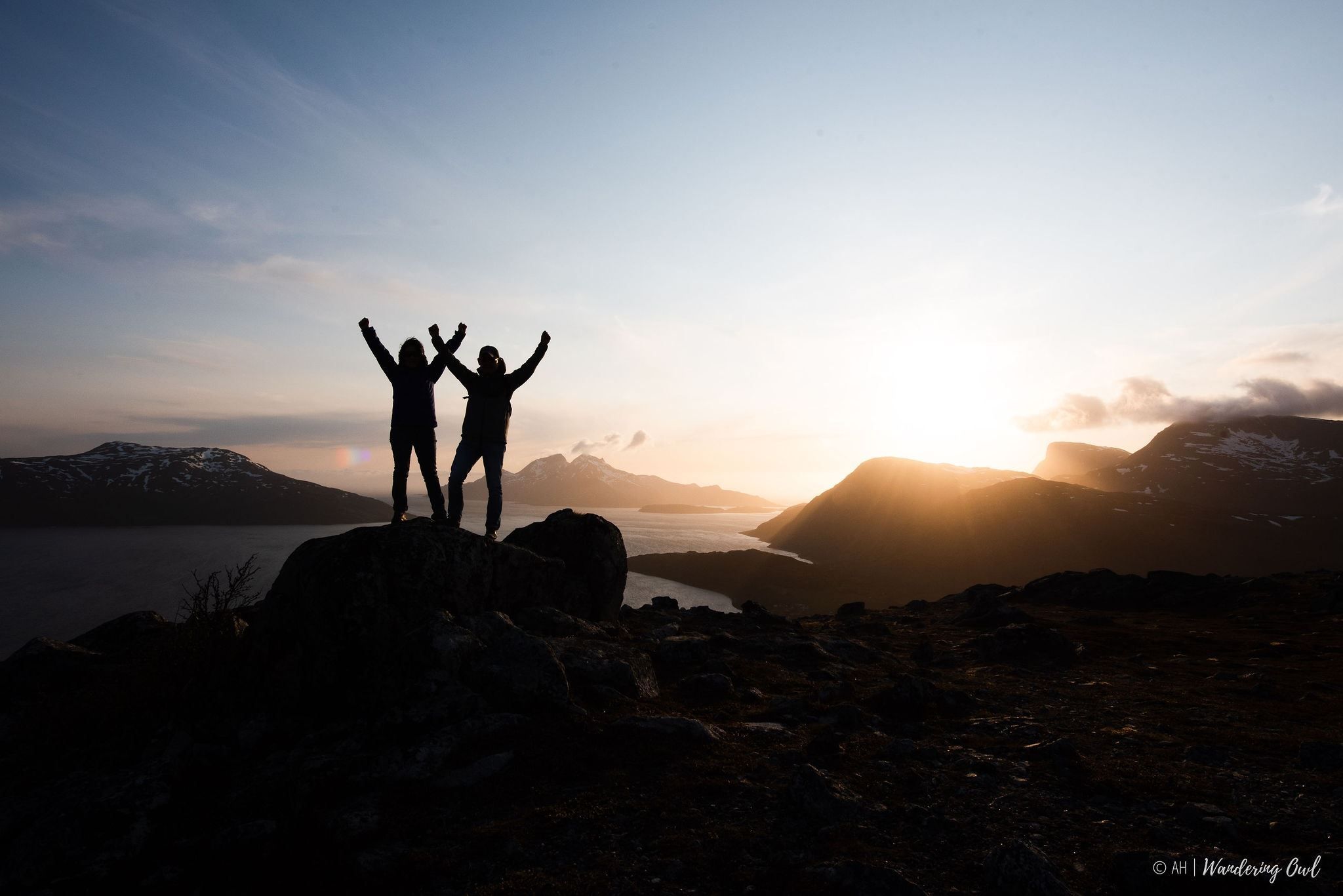 Two people raising their hands in the air in front of the midnight sun