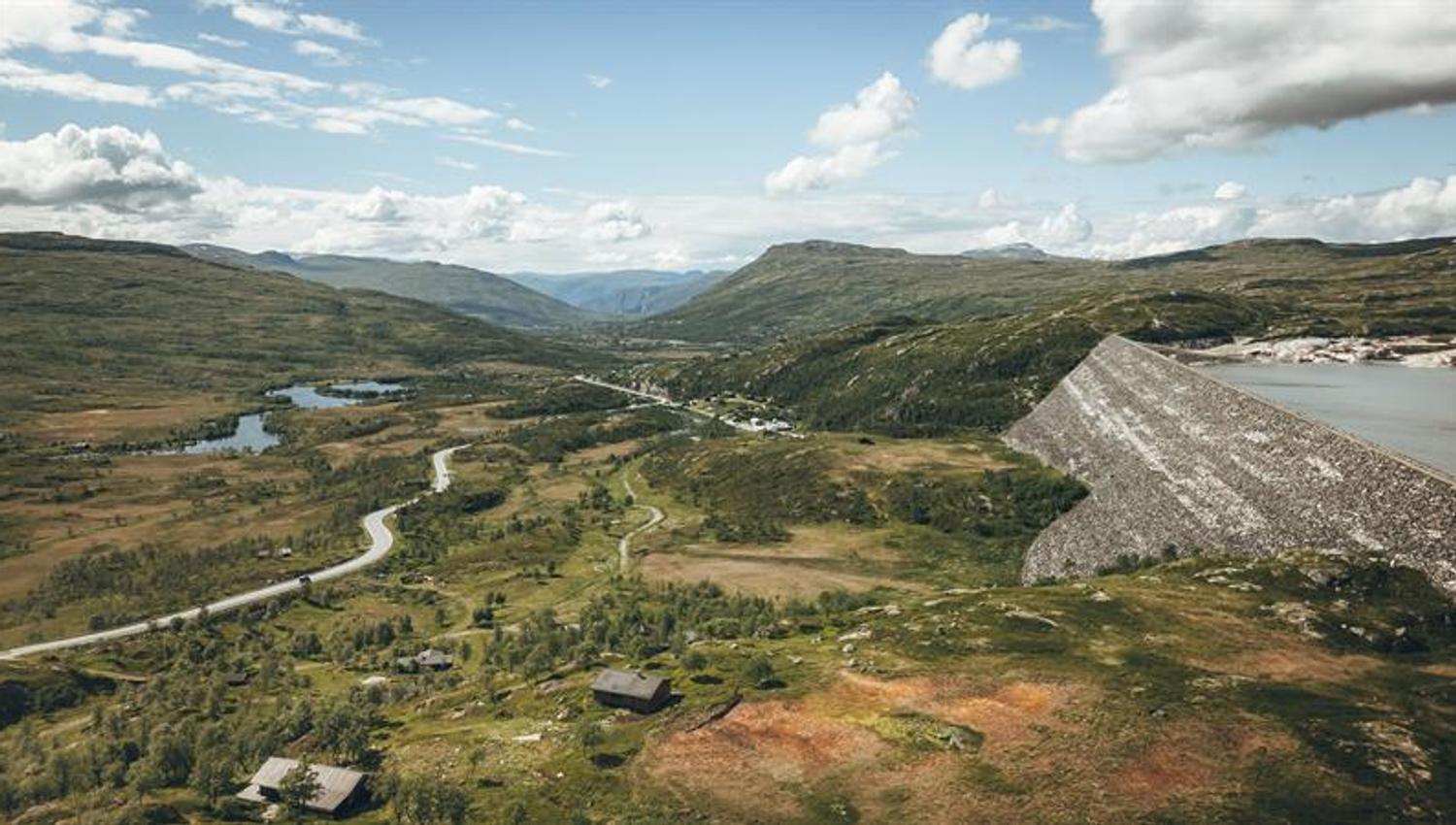 A drone photo showing the Sysendammen dam on the right and the main road and some mountain cabins on the left.