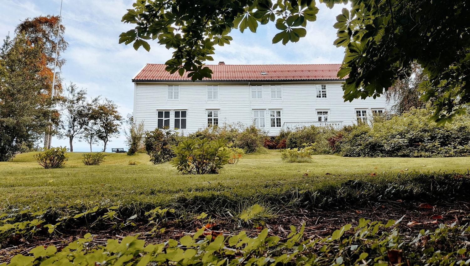 Skrivergaarden seen from the garden, surrounded by green outdoor areas with views towards the fjord.