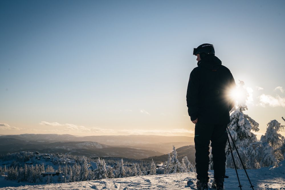 man on skis stands on a peak at Lifjell ski center and looks out over the landscape 